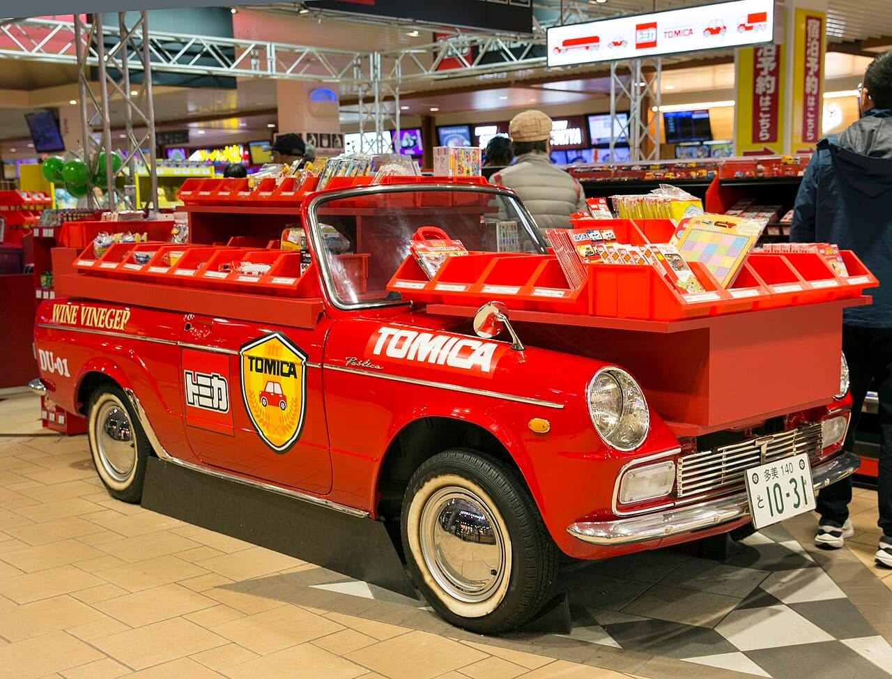 A vintage Toyota Publica repurposed as a Tomica toy display case at a Japanese highway rest stop — illustrative of the broader Tomica brand the TLV/TLV-N collector lines belong to