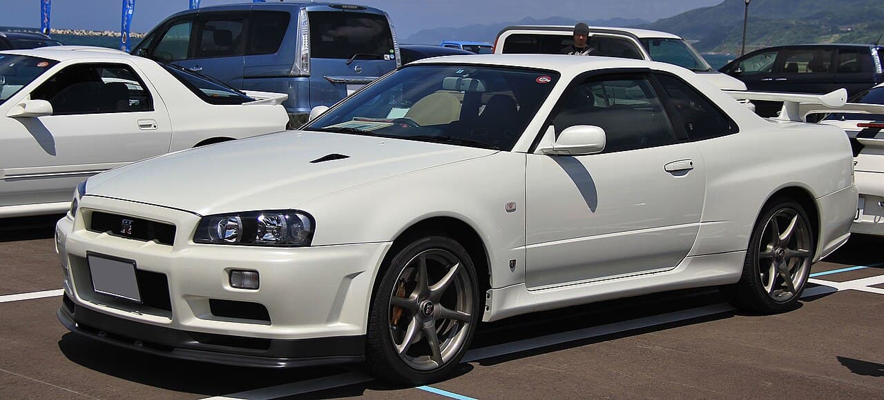 A white Nissan Skyline GT-R R34 V-Spec II parked at a car meet